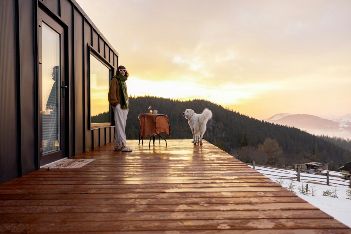 Woman with her dog resting on terrace of tiny house on nature